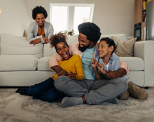 In a living room a smiling woman stands near a laughing man who is embracing two happy children.